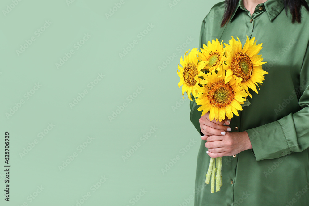 Young woman with beautiful sunflowers on green background