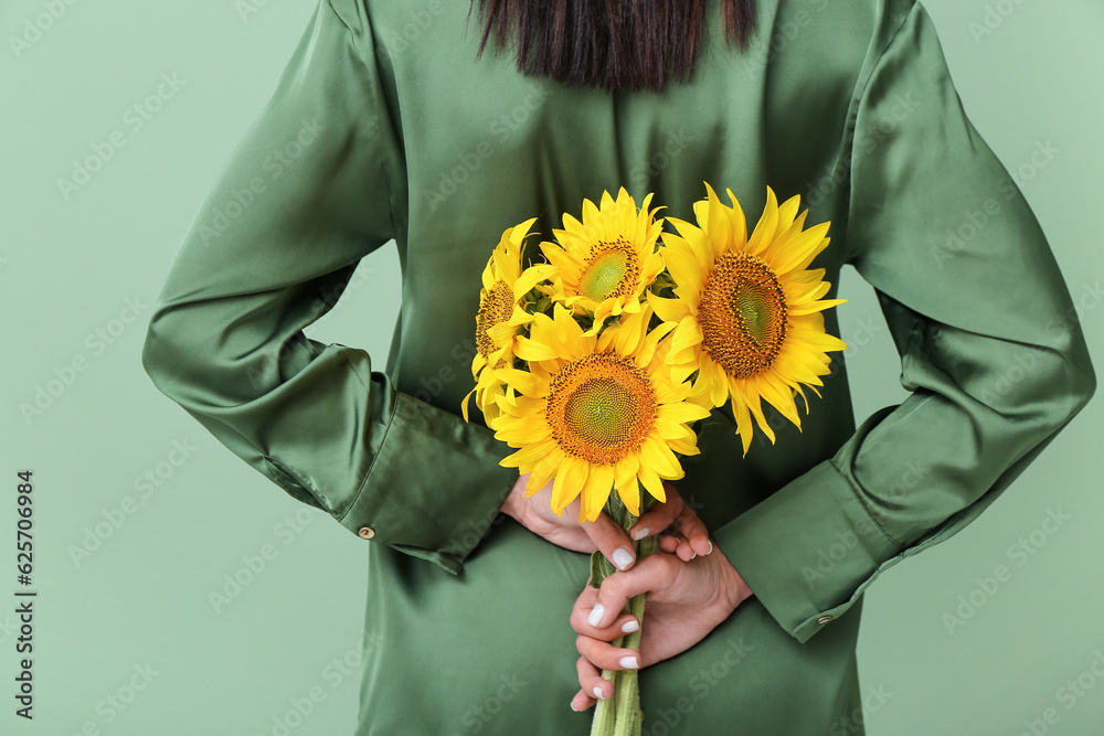 Young woman with beautiful sunflowers on green background, back view