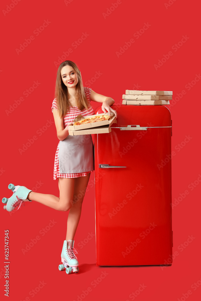 Young woman in roller skates with tasty pizza and fridge on red background