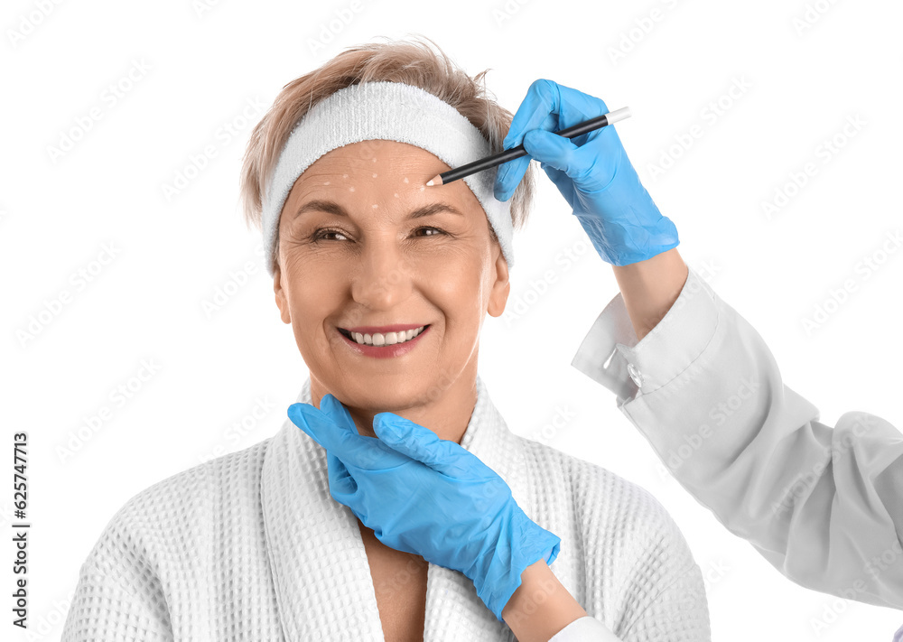 Beautician marking forehead of mature woman for filler injection on white background, closeup