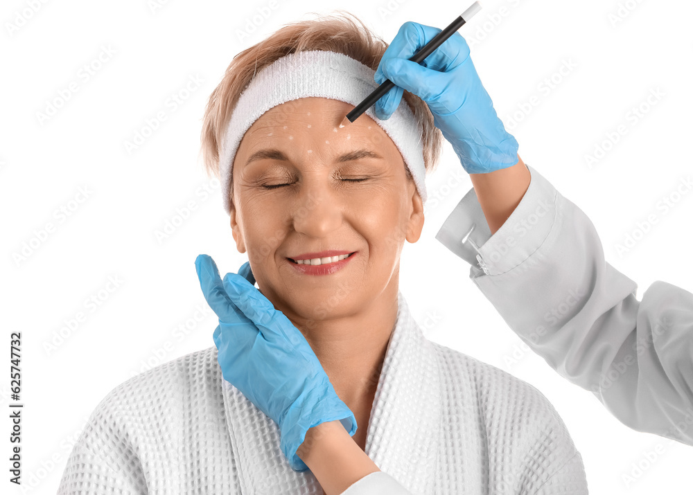 Beautician marking forehead of mature woman for filler injection on white background, closeup