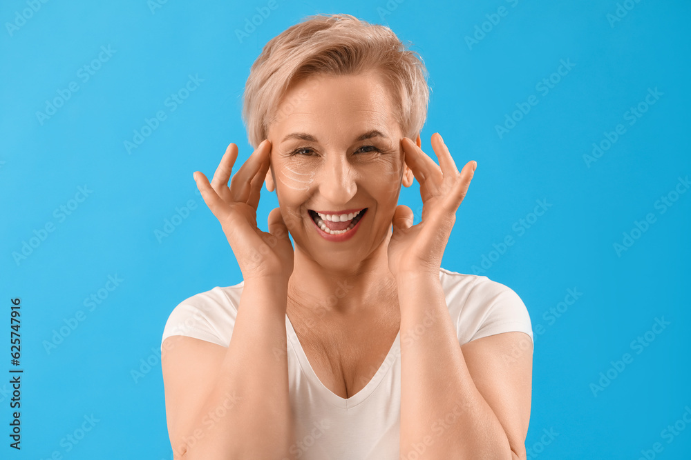 Mature woman with marked face for filler injection on blue background, closeup