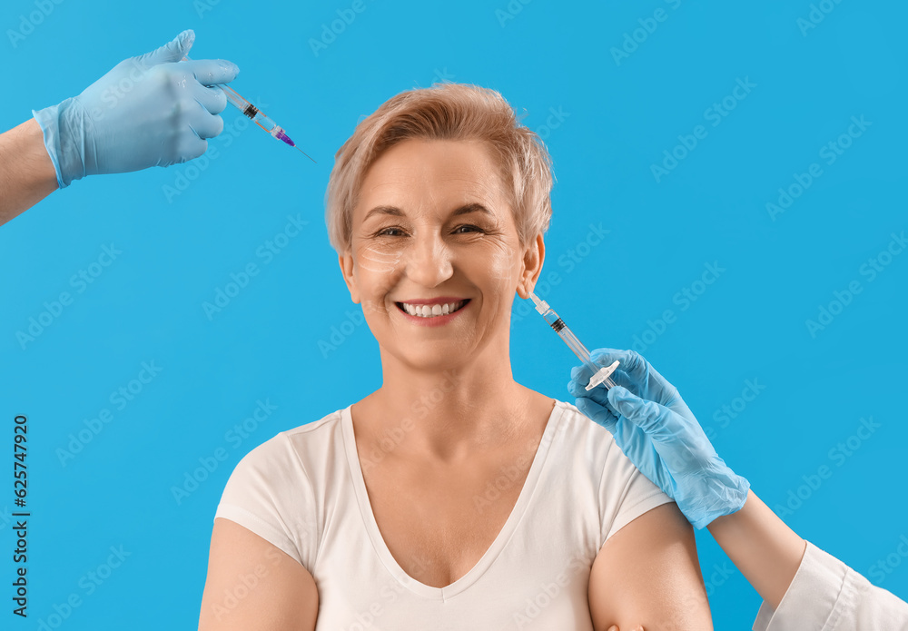 Mature woman and beauticians hands with filler injections on blue background, closeup