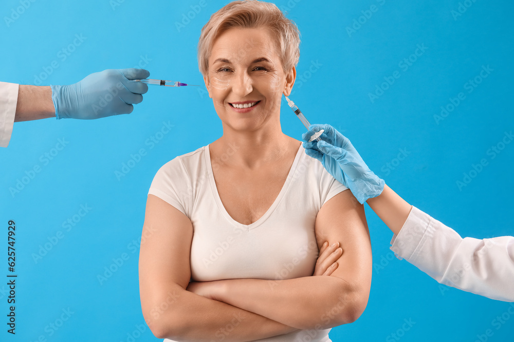 Mature woman and beauticians hands with filler injections on blue background