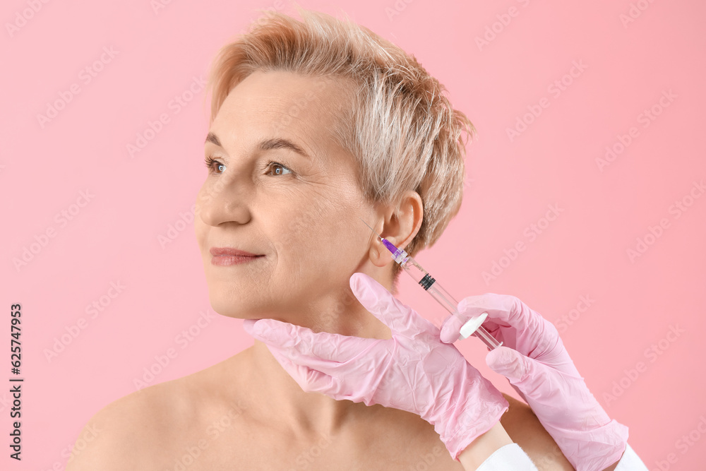 Mature woman receiving filler injection on pink background, closeup