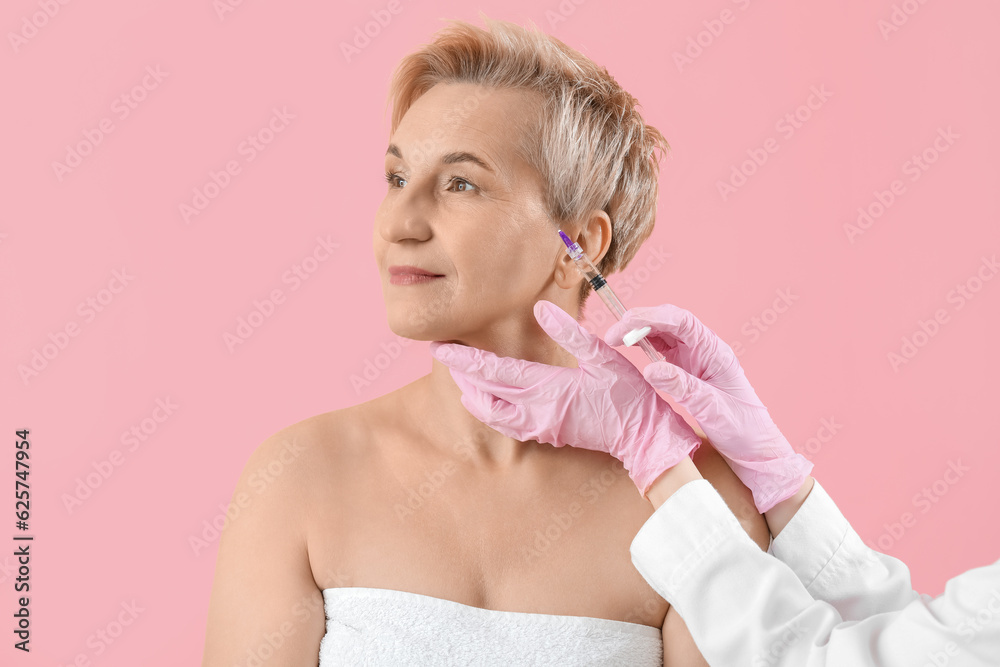 Mature woman receiving filler injection on pink background, closeup