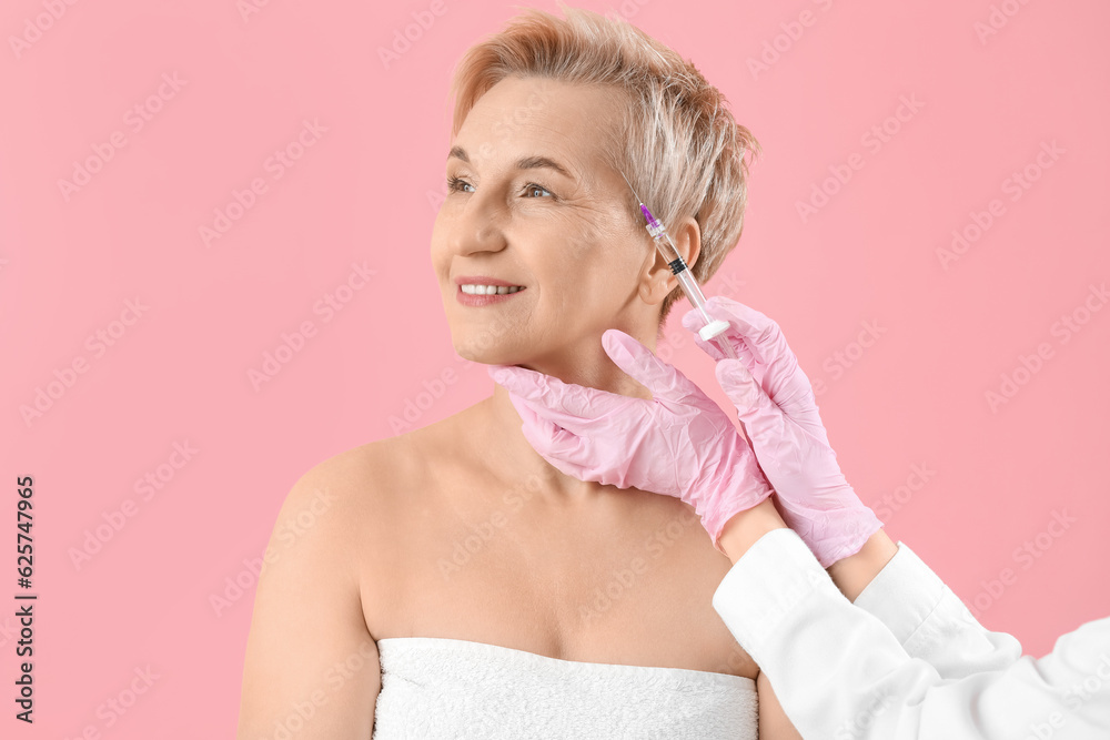 Mature woman receiving filler injection on pink background, closeup