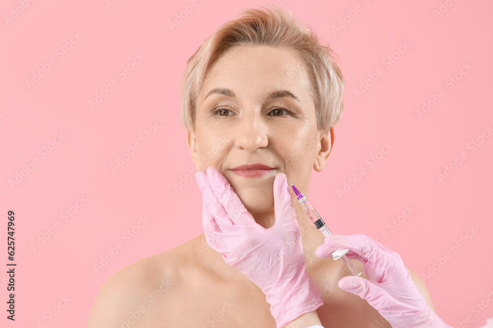 Mature woman receiving lip filler injection on pink background, closeup