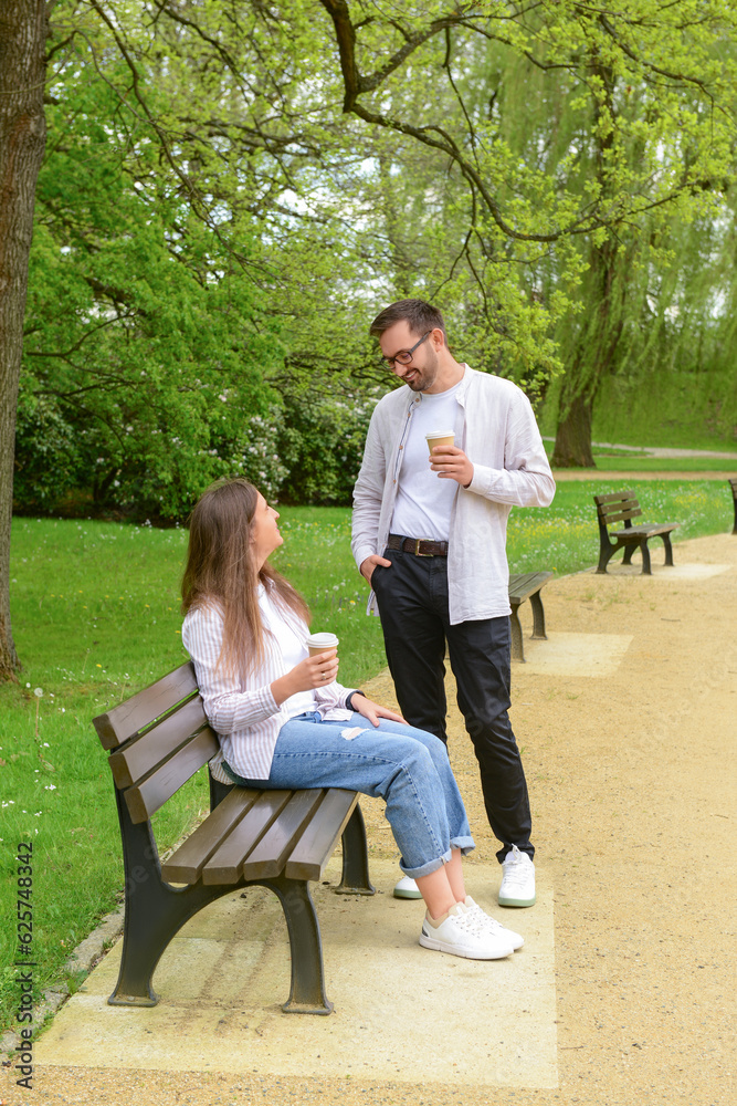 Beautiful loving couple sitting on bench and drinking coffee in park