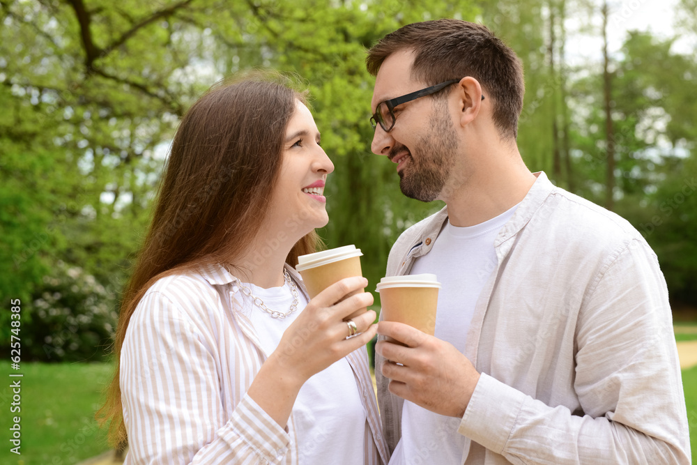 Beautiful happy loving couple walking in park and drinking coffee on spring day