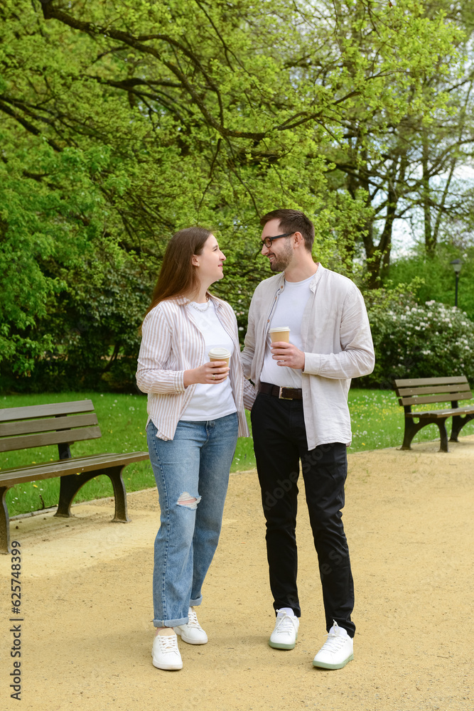 Beautiful happy loving couple walking in park and drinking coffee on spring day