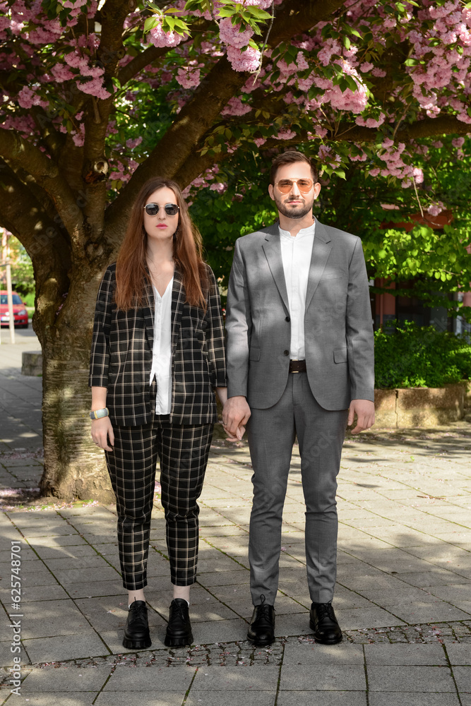 Beautiful loving young couple holding hands near blooming tree on sunny spring day