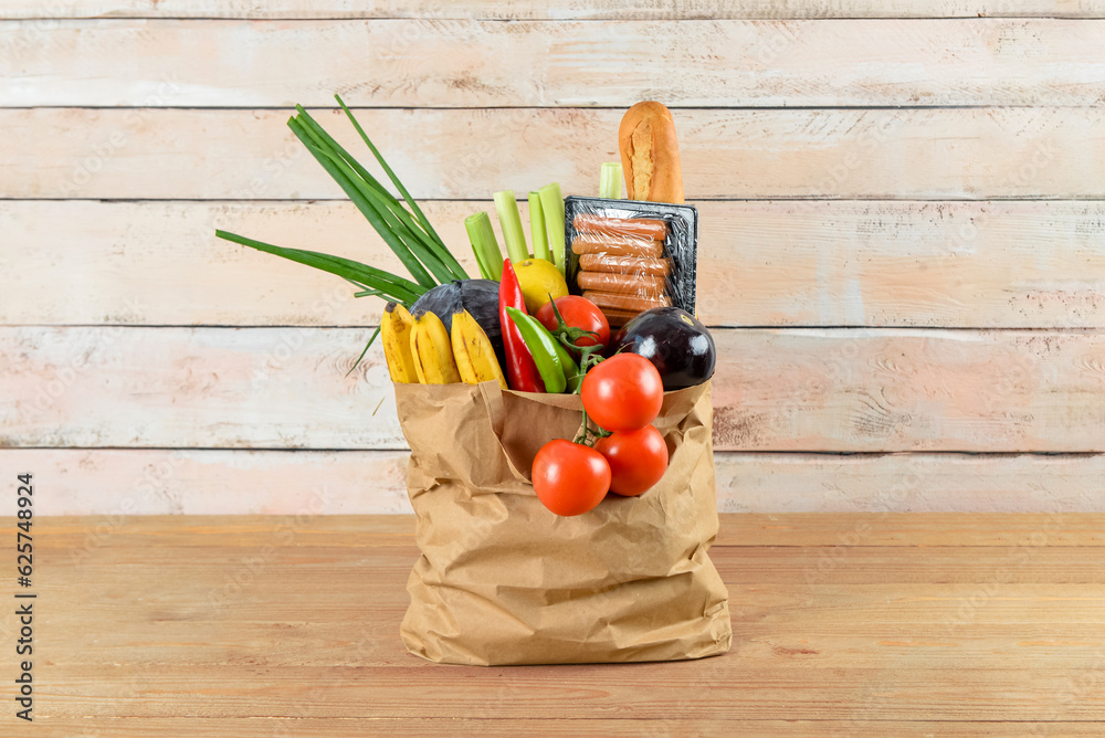 Paper bag full of fresh food on wooden table near wall. Food delivery concept