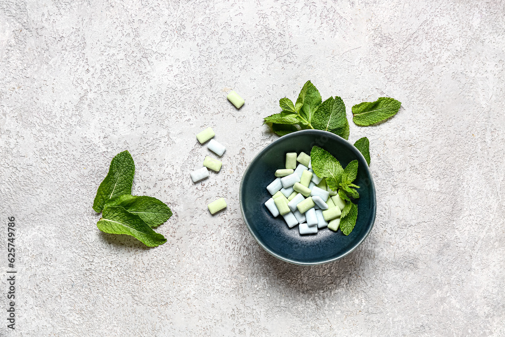 Bowl of fresh chewing gums with mint on grey background