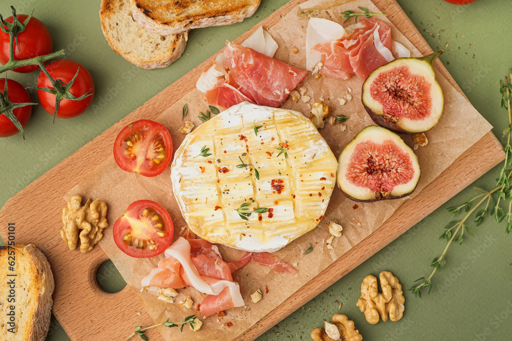 Wooden board with tasty baked Camembert cheese on green background