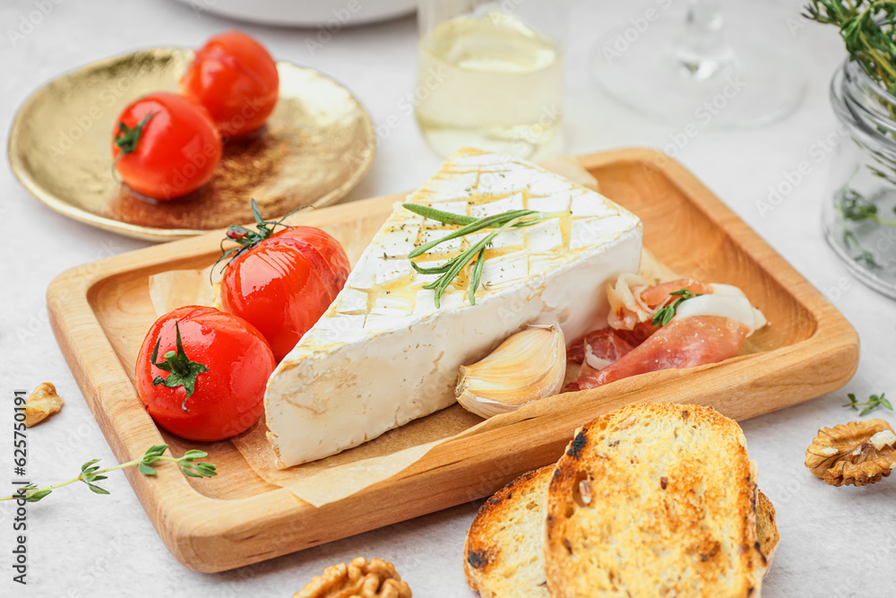 Wooden board with tasty baked Camembert cheese on light background