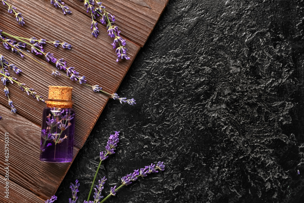 Bottle of essential oil and lavender flowers on wooden table against dark background