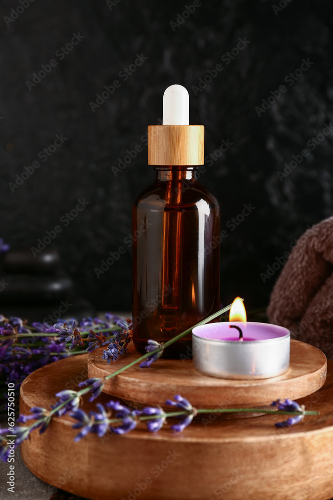 Composition with bottle of essential oil, burning candle and lavender flowers on dark background, cl