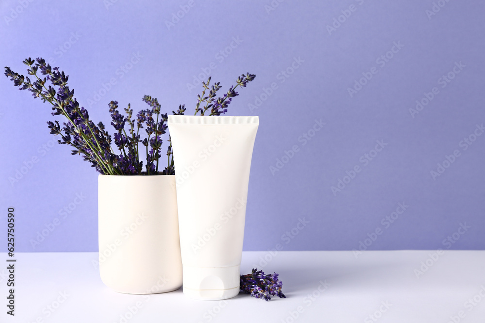 Tube of cosmetic product and lavender flowers on table against color background