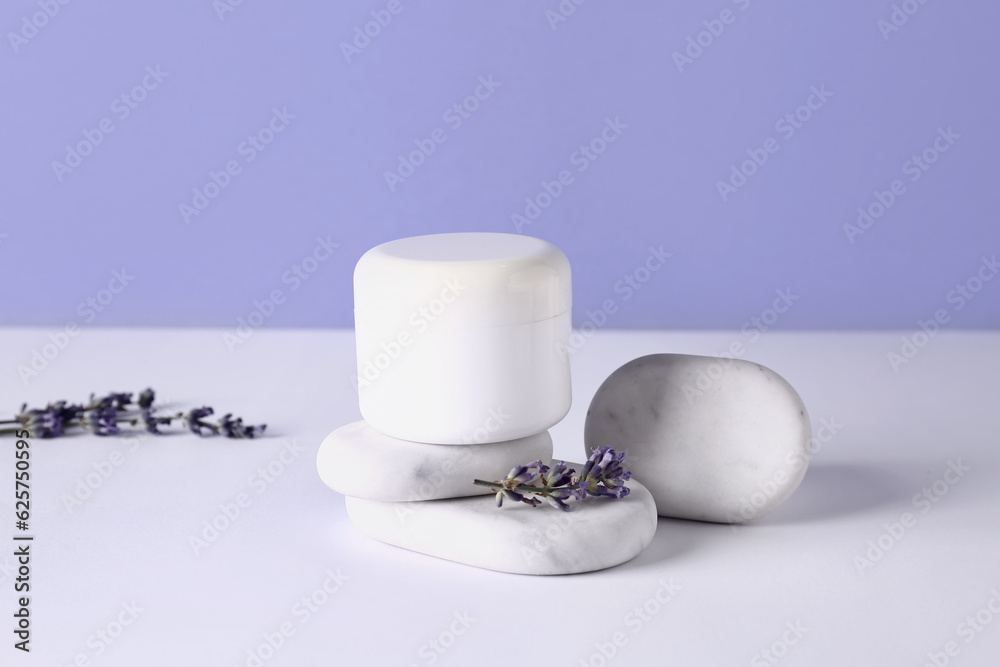 Jar of cosmetic product, spa stones and lavender flowers on light table against color background