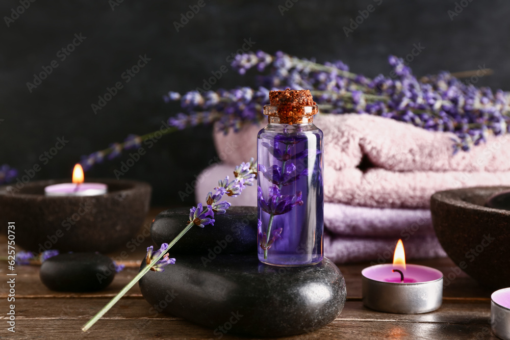 Composition with bottle of essential oil, spa stones, burning candles and lavender flowers on wooden