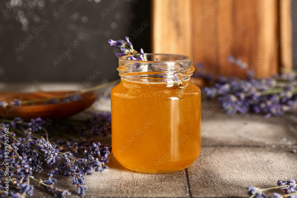 Jar of sweet lavender honey and flowers on grey tile table