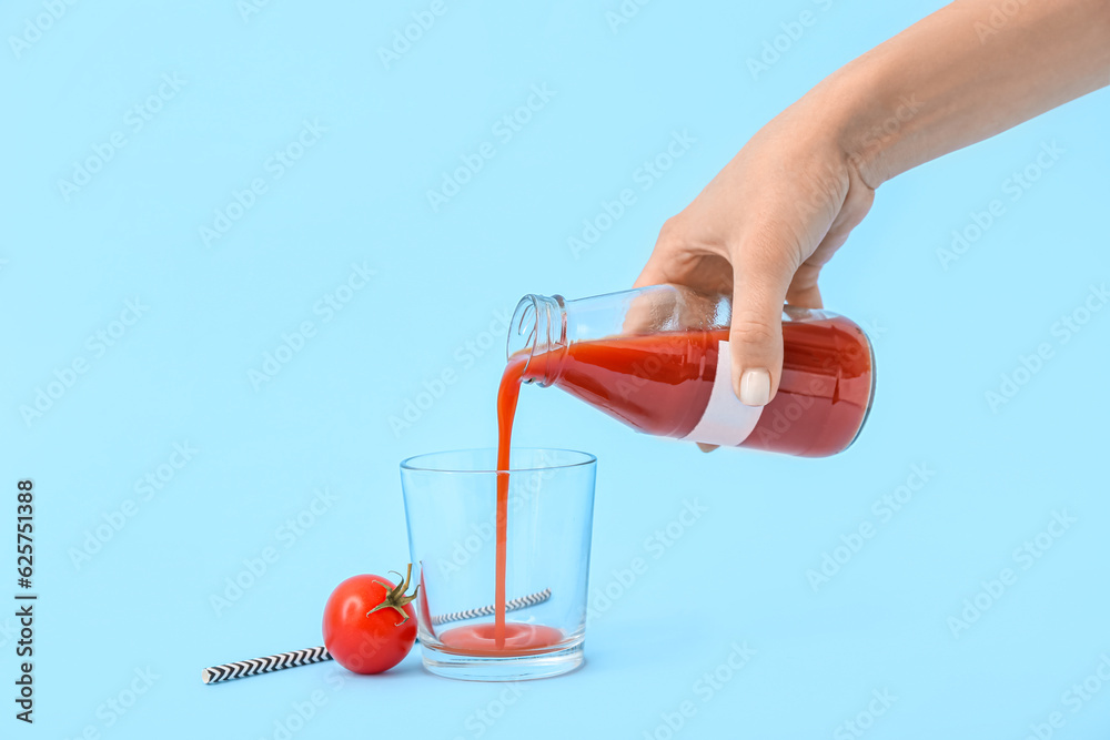 Woman pouring tasty tomato juice from bottle into glass on blue background