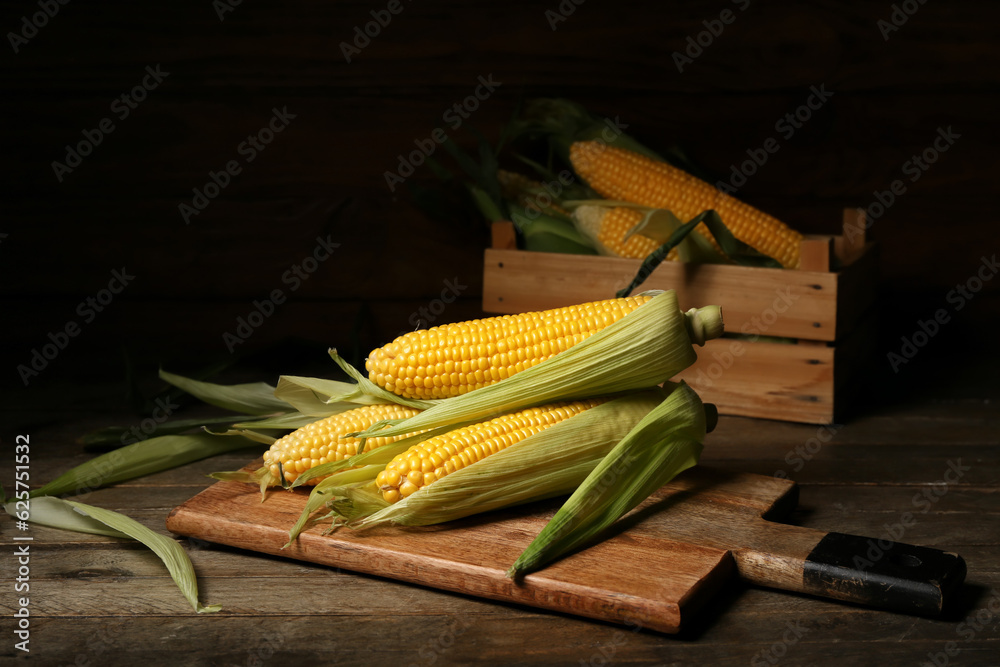 Board and box with fresh corn cobs on wooden table