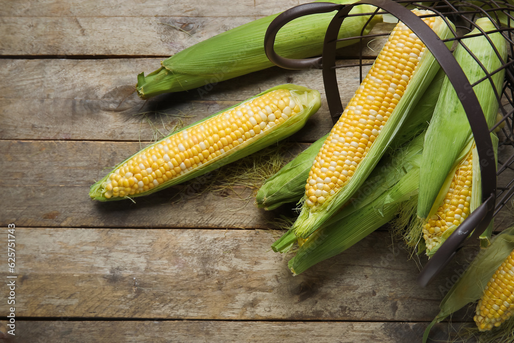 Basket with fresh corn cobs on wooden background