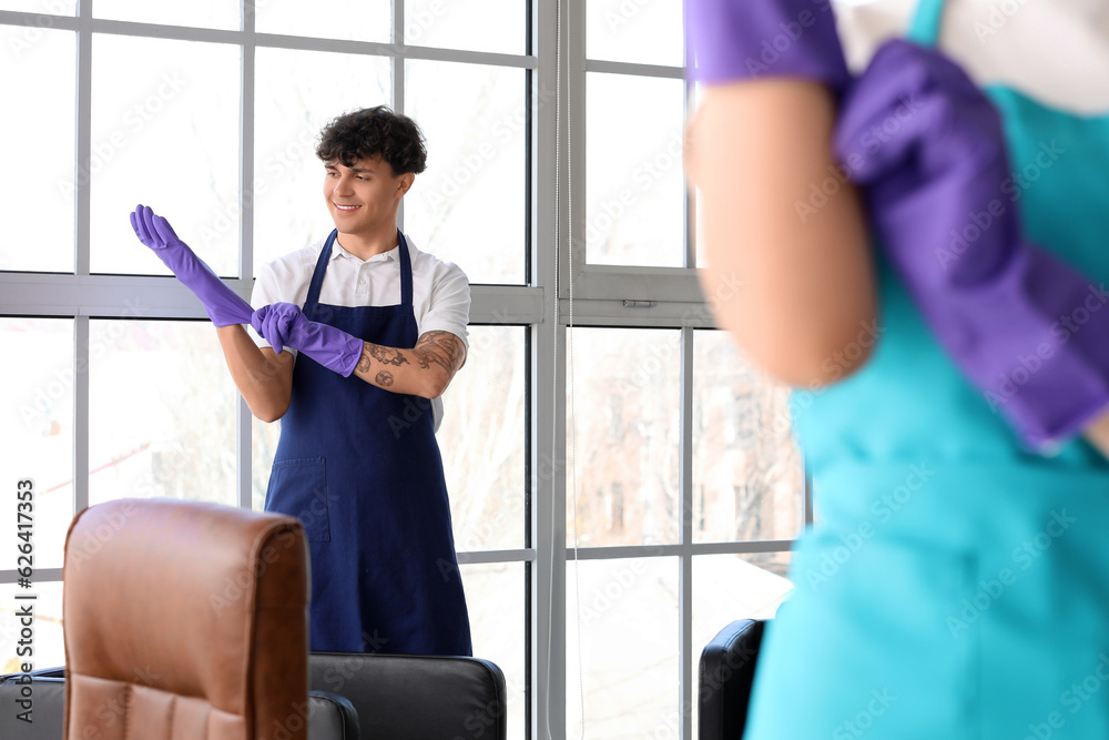 Male janitor putting rubber gloves in office