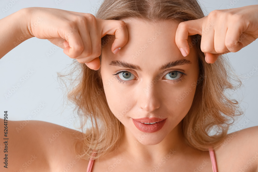 Young woman doing face building exercise on light background, closeup