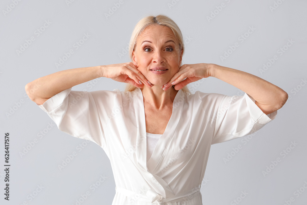 Mature woman doing face building exercise on light background