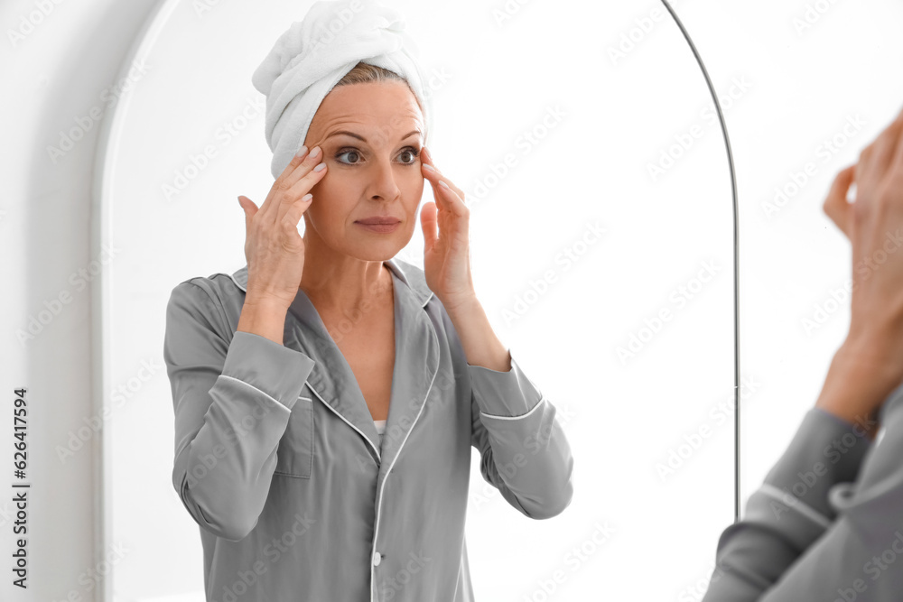 Mature woman doing face building exercise near mirror in bathroom