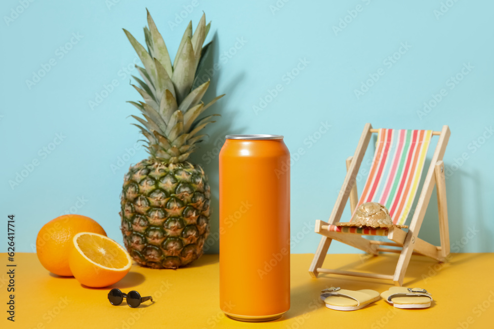 Can of soda with beach decor and fruits on table near blue wall