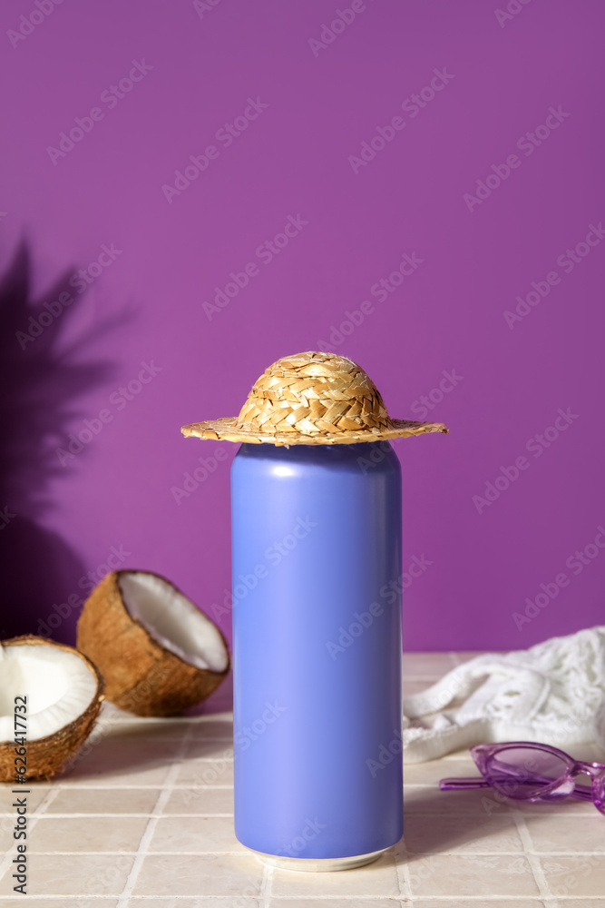 Can of soda with beach hat and coconut on table near purple wall