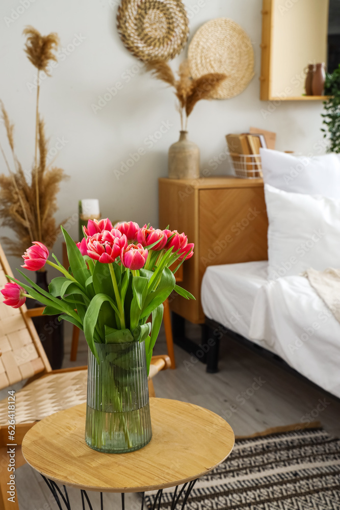 Vase with blooming tulip flowers on table in bedroom