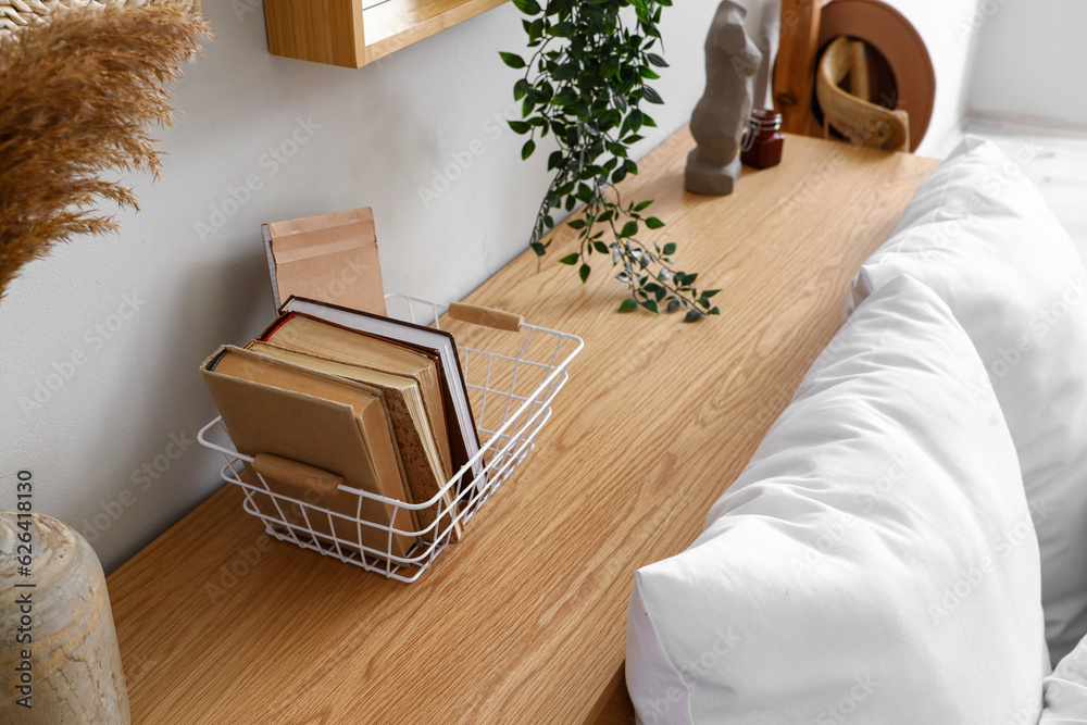 Wooden table with houseplant, books and decorative figurine near bed, closeup