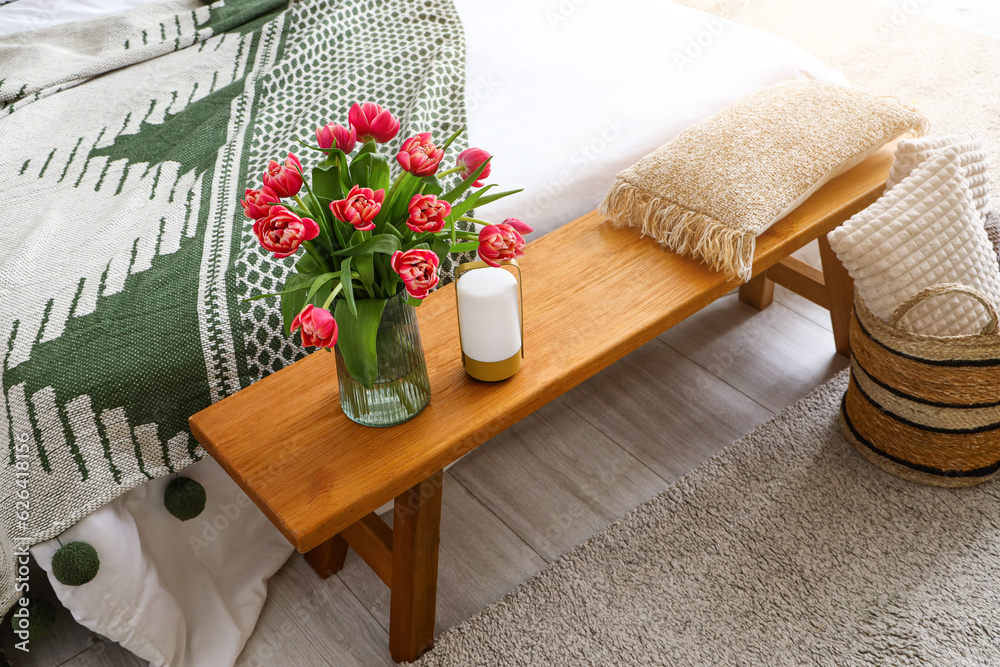 Vase with blooming tulips on wooden bedside bench in bedroom