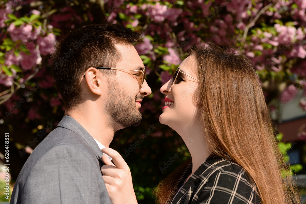 Beautiful loving couple hugging near blooming tree on sunny spring day