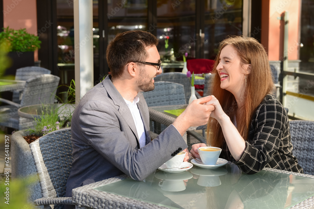 Beautiful happy loving couple sitting in restaurant, drinking coffee and holding hands on sunny spri