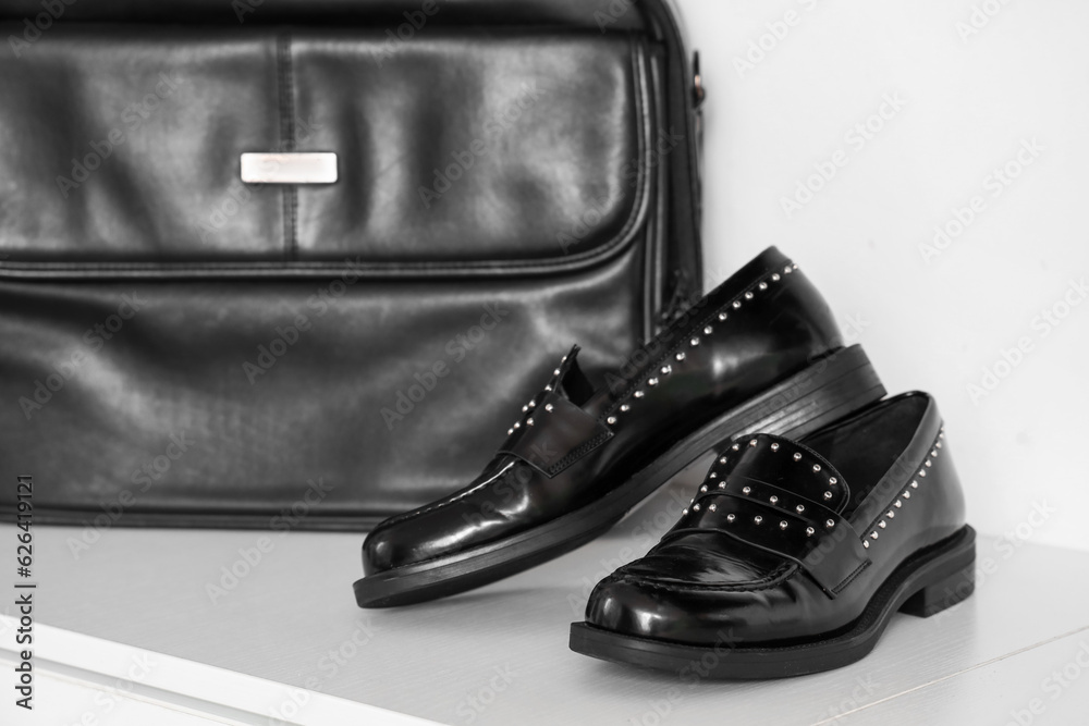 Stylish black shoes and bag on shelf in boutique, closeup