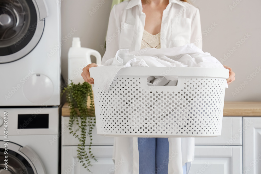 Woman with basket of dirty clothes in laundry room with washing machines