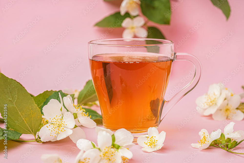 Glass cup of tea and beautiful jasmine flowers on pink background