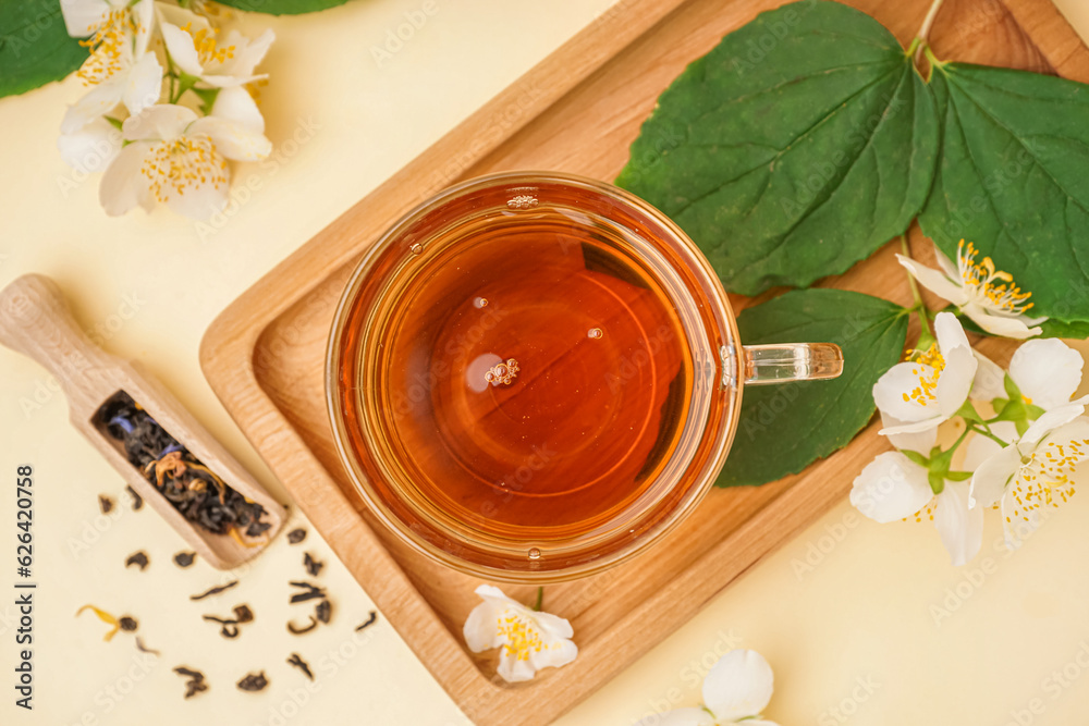 Cup of aromatic tea, dried leaves and beautiful jasmine flowers on color background, closeup