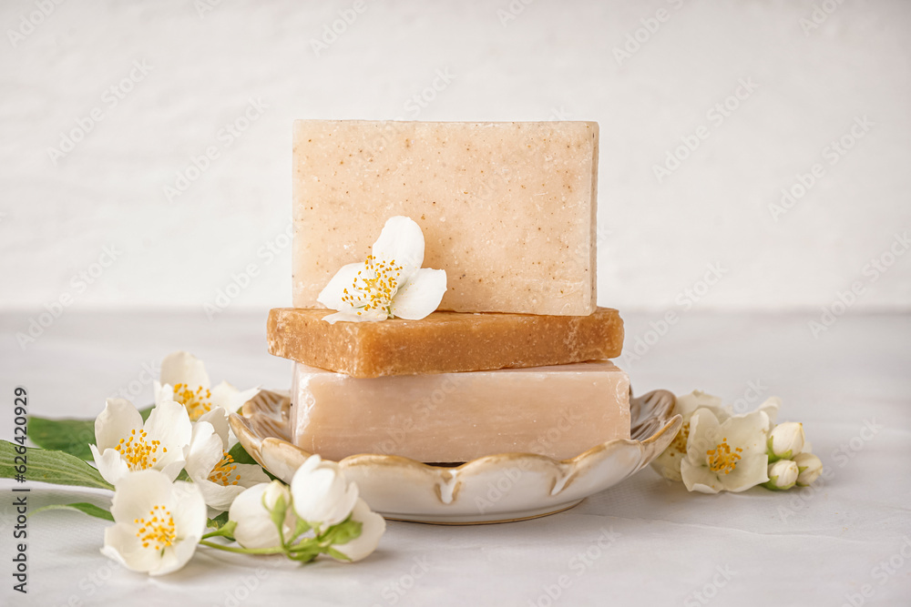 Stack of soap bars and beautiful jasmine flowers on light background