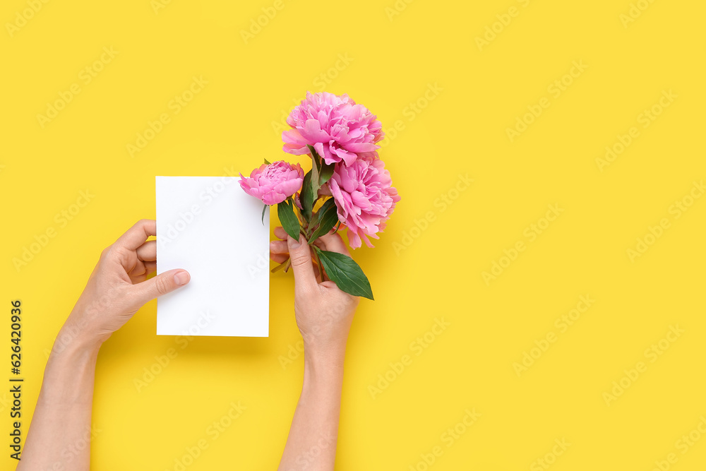 Female hands with blank card and beautiful peony flowers on yellow background