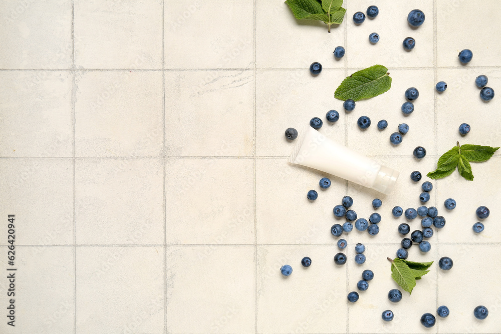 Composition with cosmetic product, mint and blueberry on light tile background