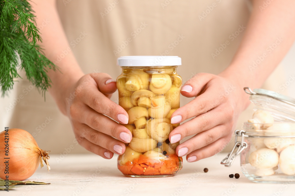 Woman holding jar with canned mushrooms at table