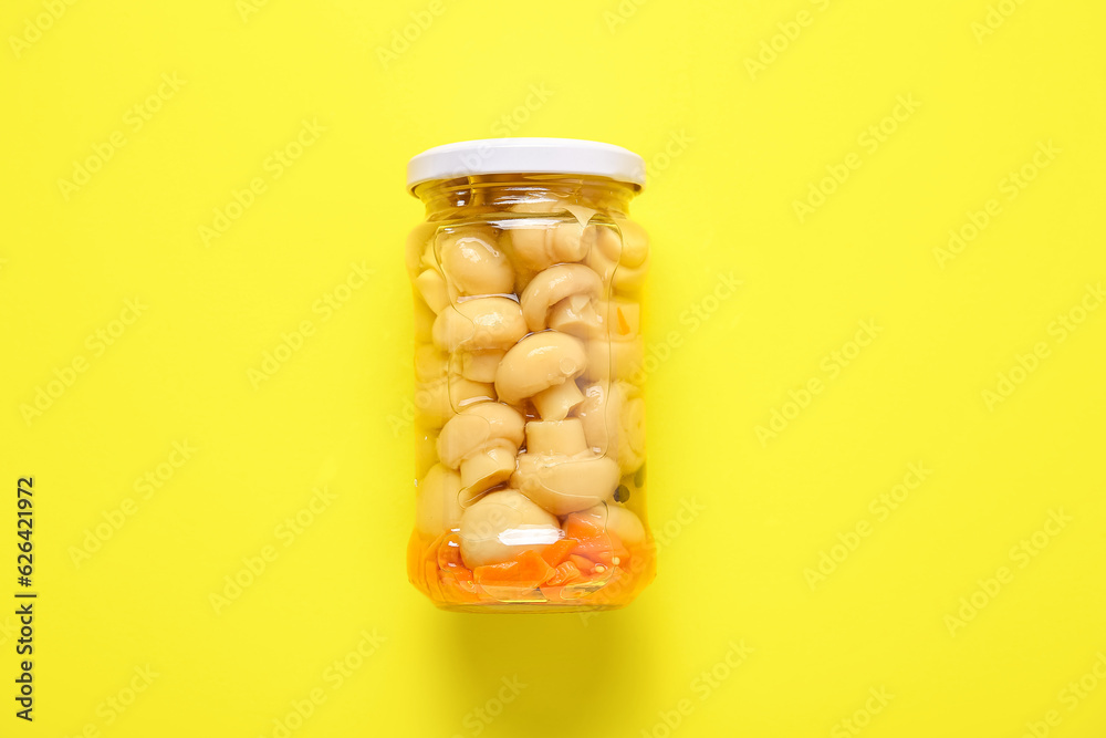 Jar with canned mushrooms on yellow background