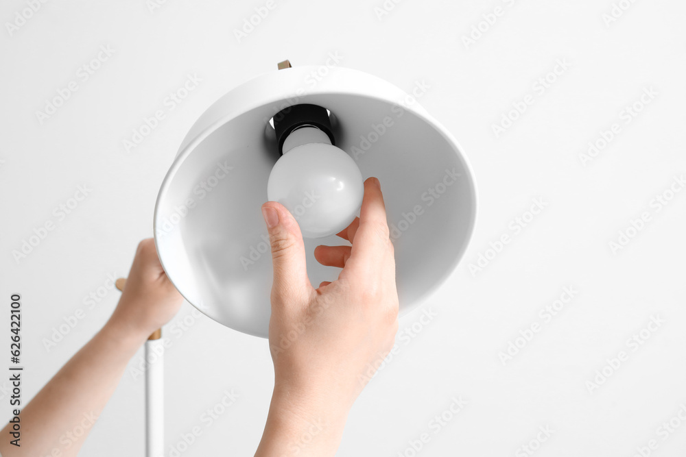 Woman changing light bulb in lamp on light background, closeup